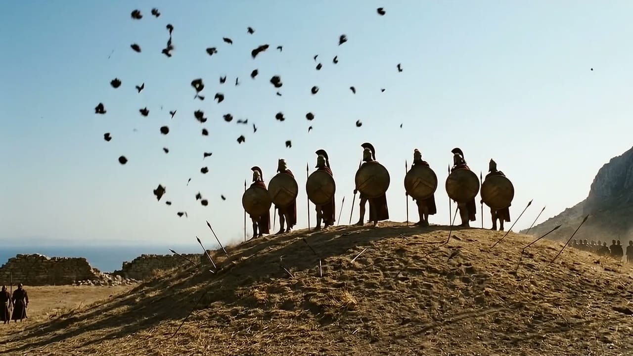 Siete hoplitas de espaldas en lo alto de una colina baja, con los escudos al hombro, mientras un enjambre de proyectiles cruza el cielo y otros quedan clavados en el suelo.